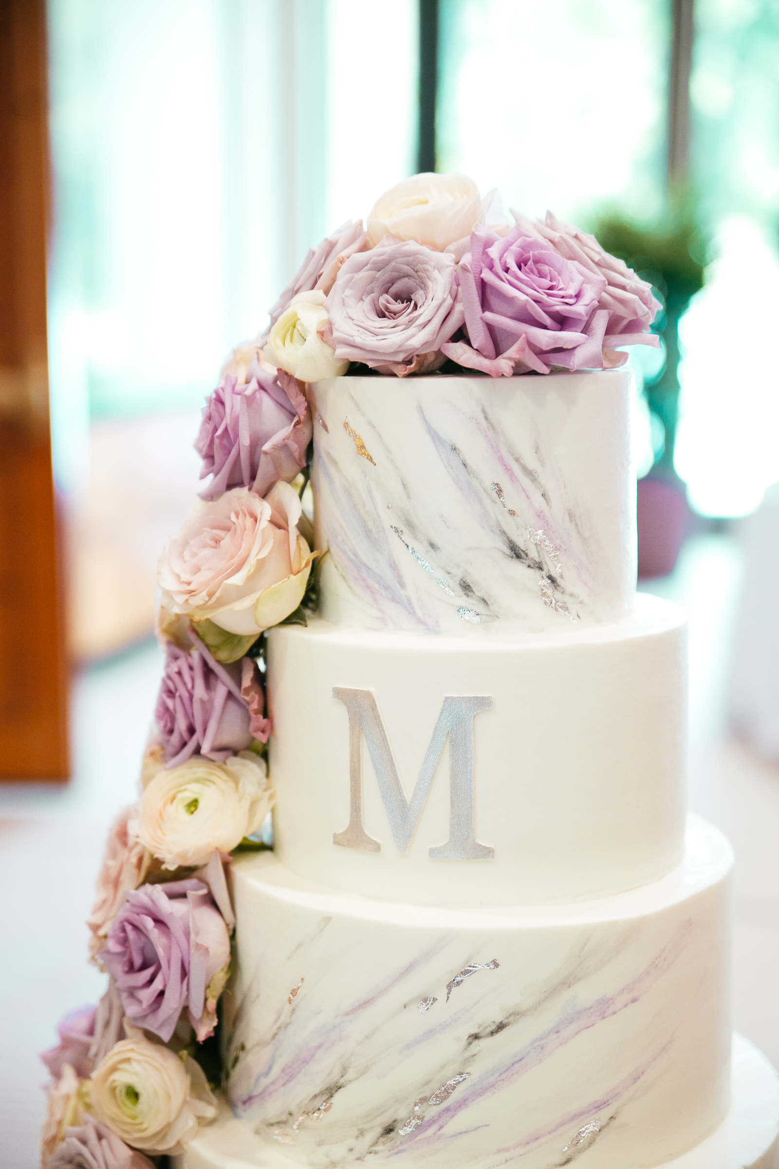 modern buttercream wedding cake with marbling in purple and silver monogram with fresh flower cascade at the Umstead Hotel and Spa
