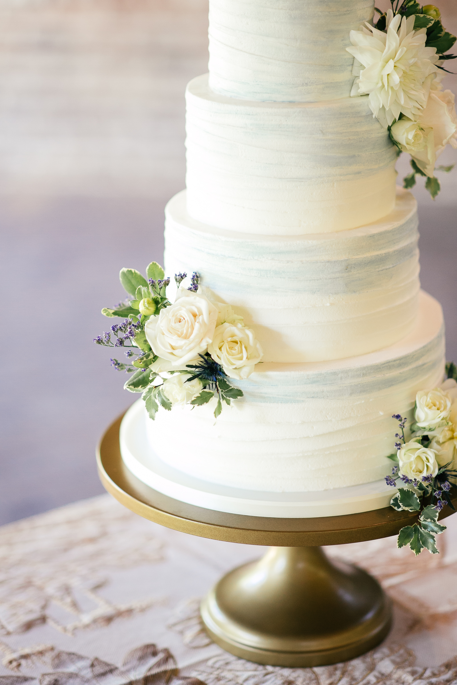 hand painted wedding cake with dusty blue watercolor accents and fresh flowers on gold cake stand
